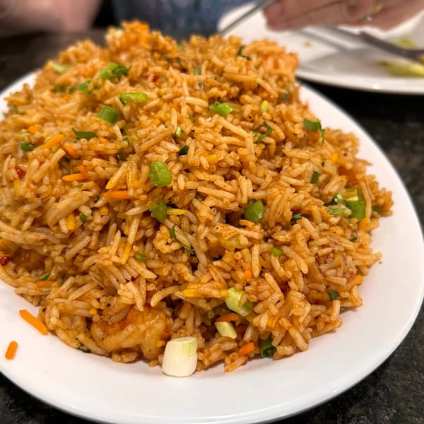 A large plate of Indian fried rice with vegetables and shrimp, garnished with green onions.