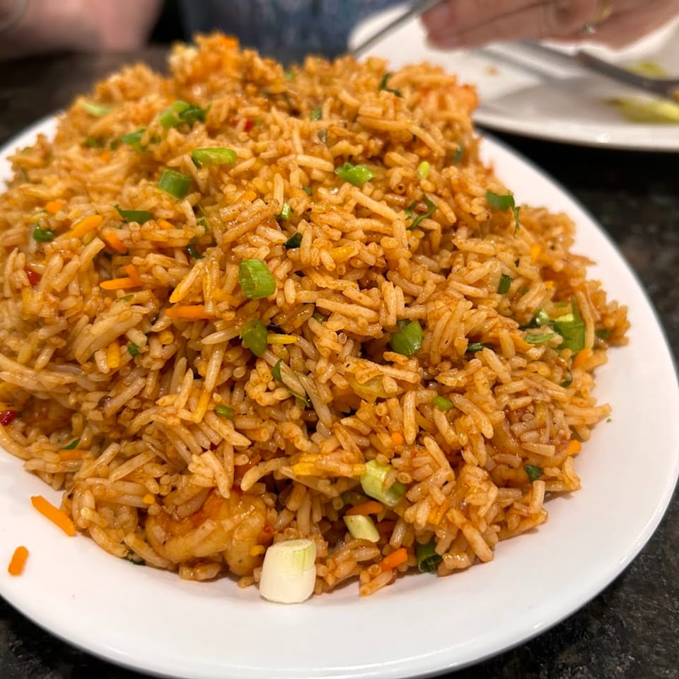 A large plate of Indian fried rice with vegetables and shrimp, garnished with green onions.