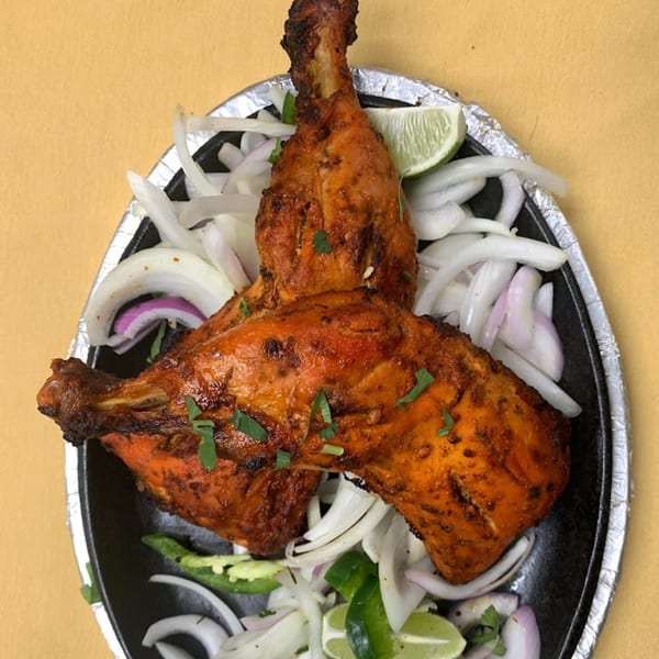 Two Bombay Curry Tandoori chicken drumsticks with sliced onions, green chilies, and lime wedges.