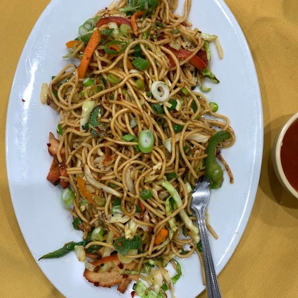 A plate of Indian noodles with chicken and vegetables, including carrots, cabbage, and green onions.