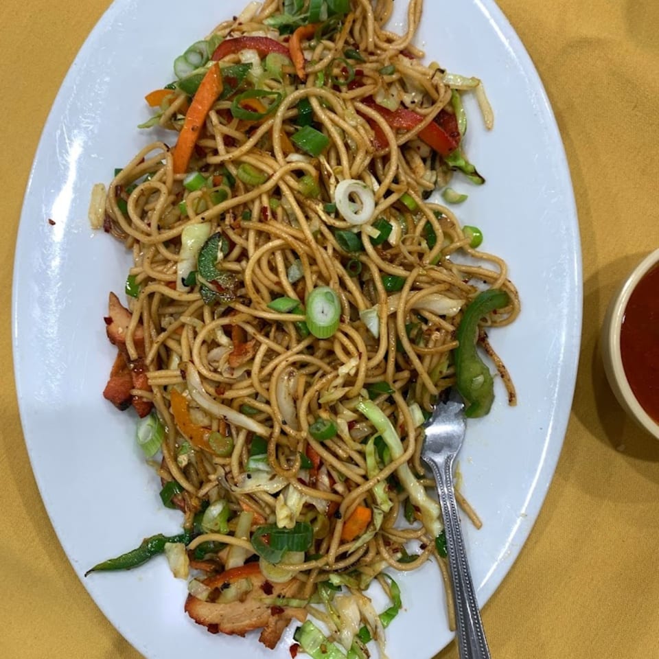 A plate of Indian noodles with chicken and vegetables, including carrots, cabbage, and green onions.