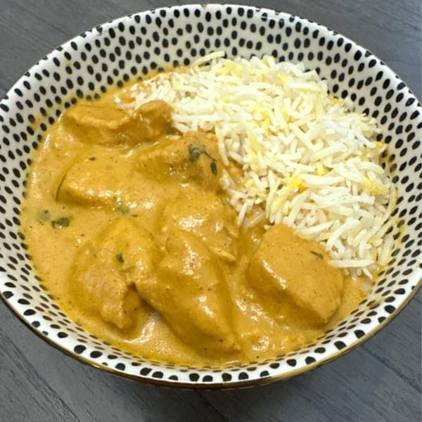 A bowl of Indian butter chicken with rice, served in a black and white polka dot bowl.
