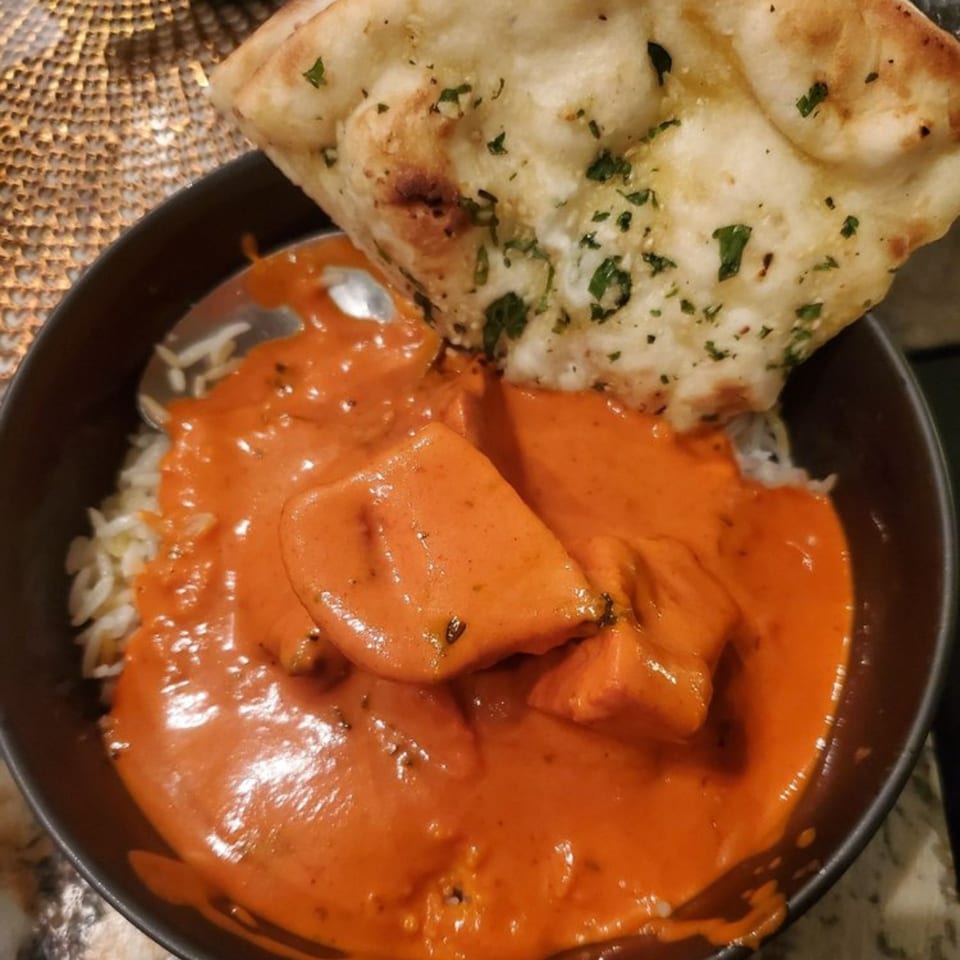 A bowl of Bombay Curry's chicken tikka masala with rice and a piece of naan bread.